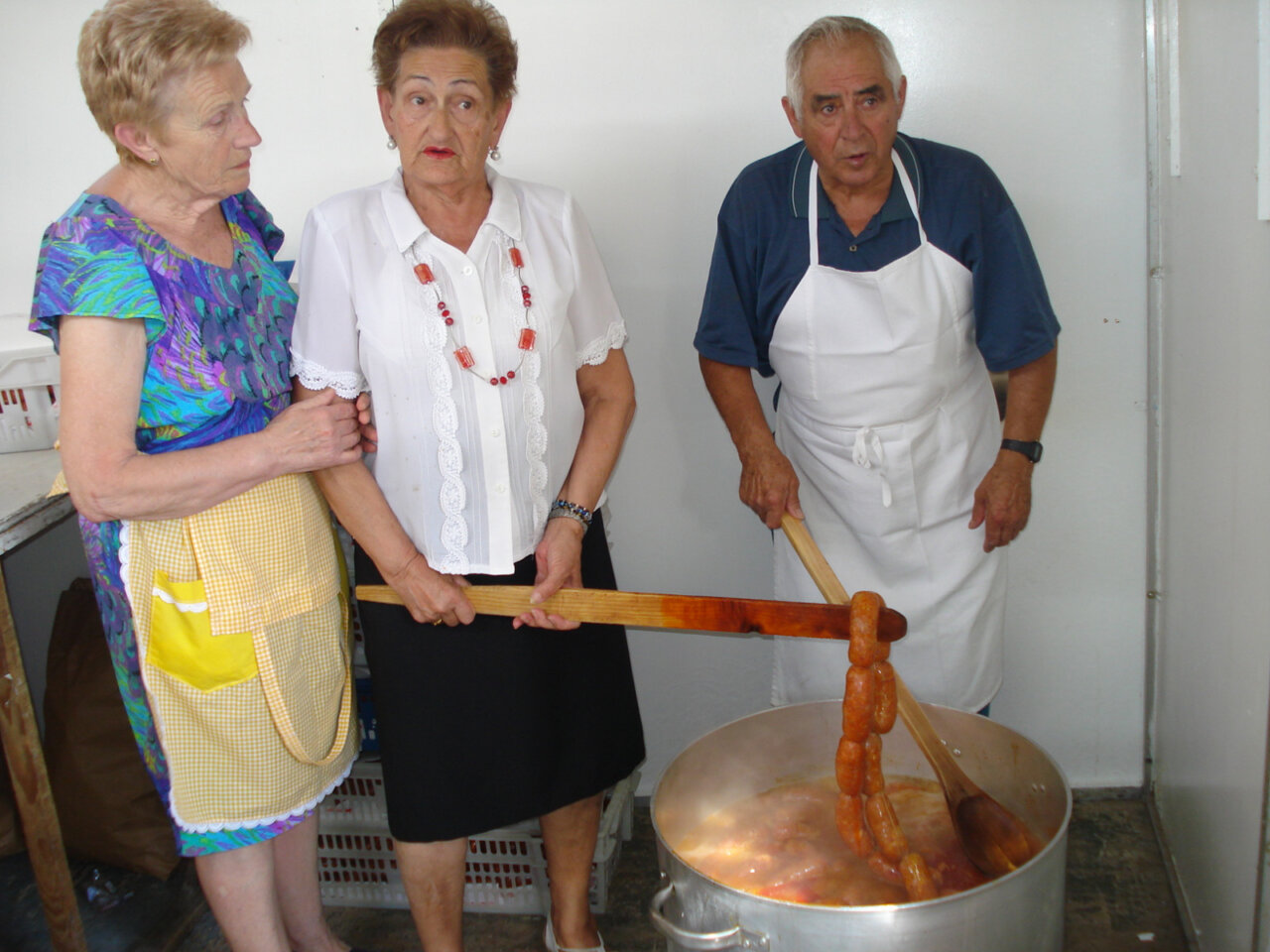 Tres personas cocinando en una olla grande durante las fiestas del barrio