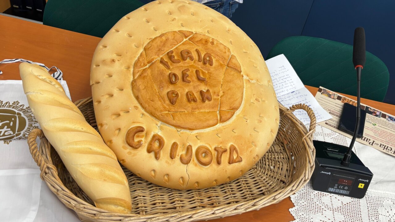 Pan grande con el texto Feria del Pan Grijota y una barra de pan en una cesta