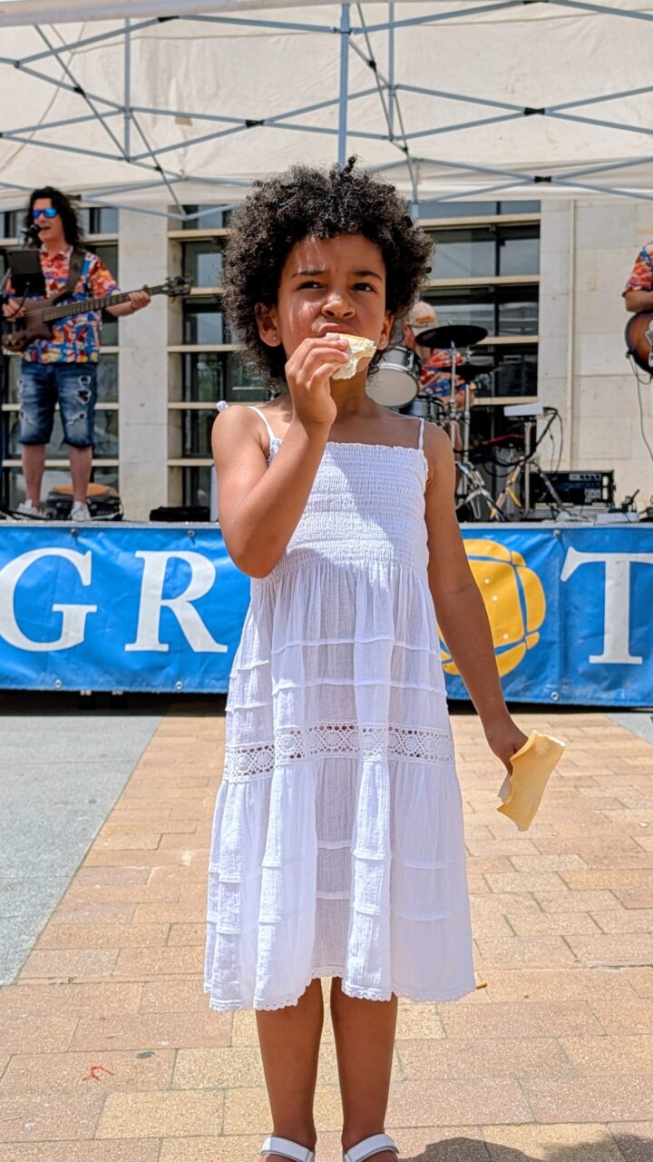 Niña pequeña con vestido blanco comiendo un trozo de pan en la feria del pan.