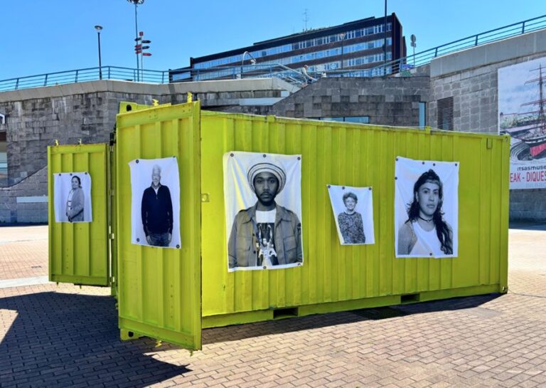 Contenedor amarillo con retratos en el Museo Migrante en Palencia