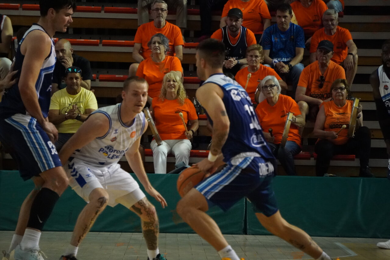 Jugadores de baloncesto en acción con aficionados en el fondo