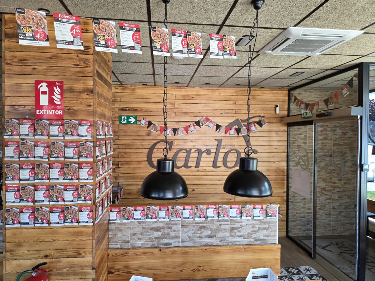 Interior de la Pizzería Carlos con decoración y promociones de pizzas