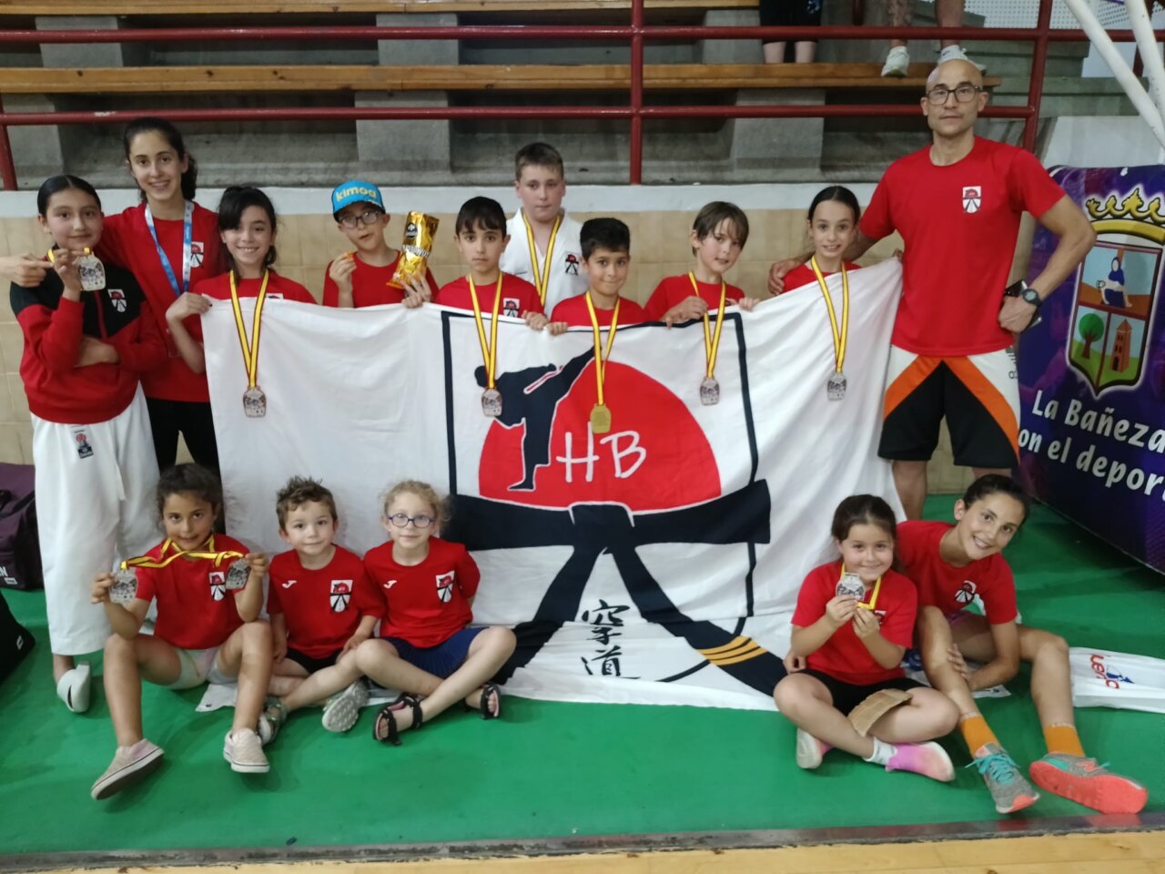 Grupo de jóvenes karatecas con medallas y bandera del club en La Bañeza