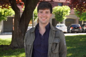 Joven sonriente en un parque con árboles y coches de fondo