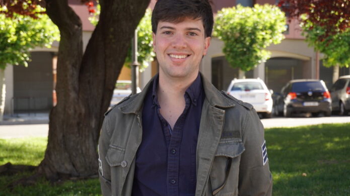 Joven sonriente en un parque con árboles y coches de fondo