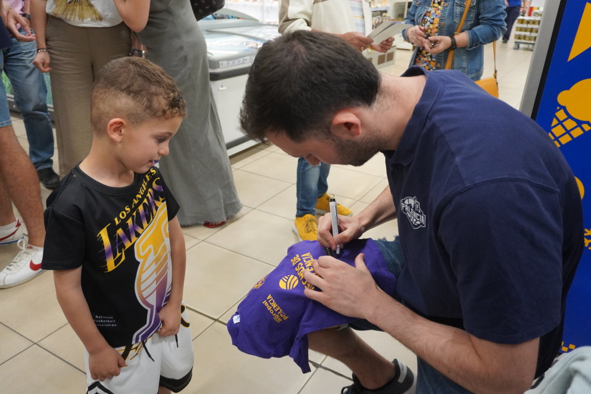 Un niño observa mientras un adulto firma una camiseta en un evento