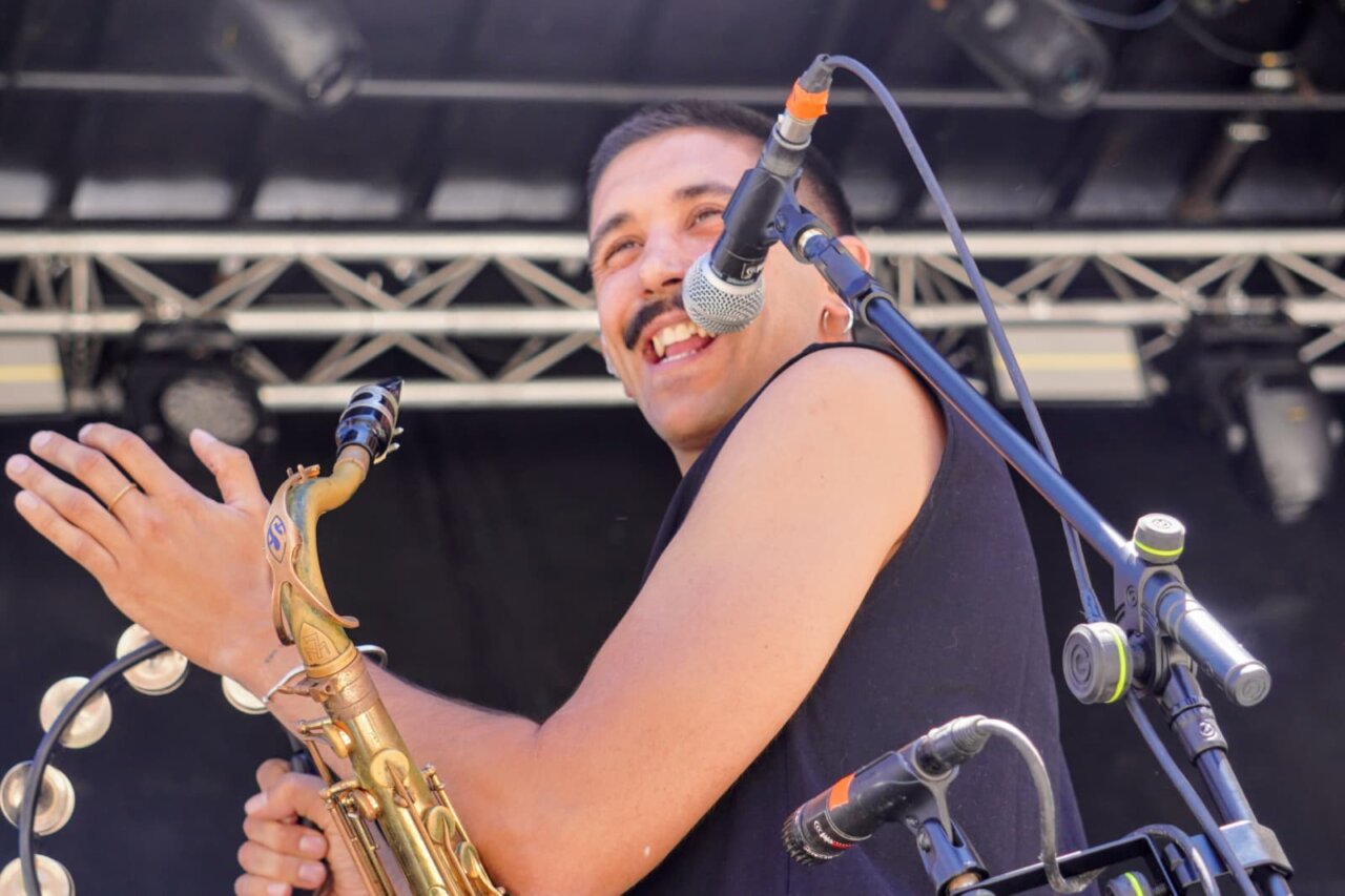 Músico sonriendo mientras toca un saxofón en un festival