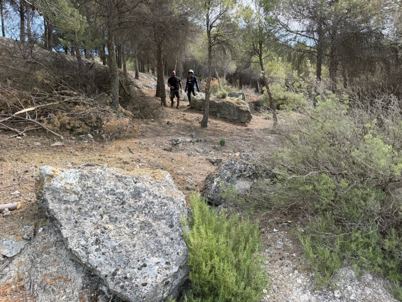 Dos personas caminando por un sendero rocoso en un bosque.