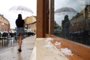 Mujer con paraguas caminando en una calle lluviosa con granizo