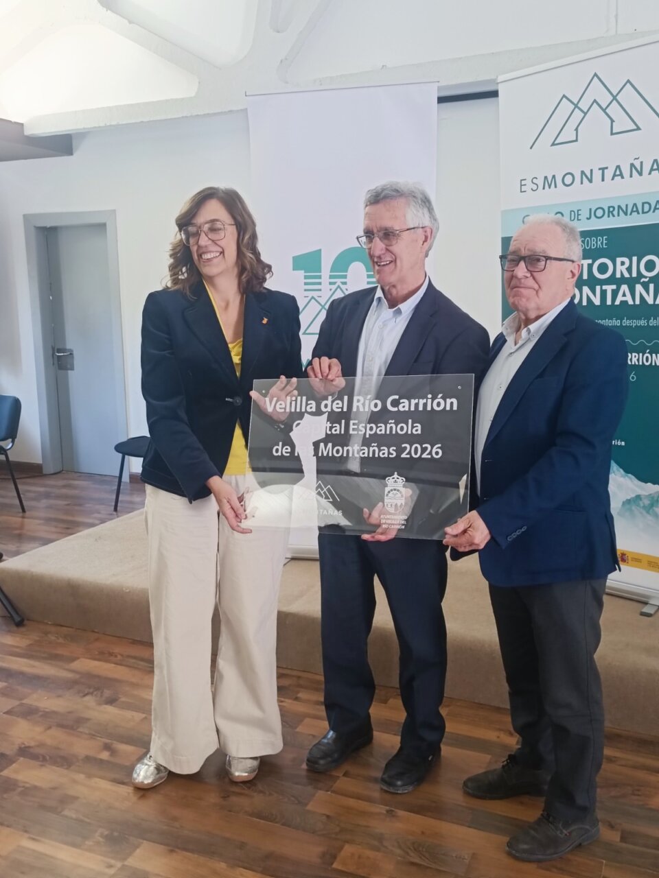 Tres personas sosteniendo un cartel de Velilla del Río Carrión como Capital Española de las Montañas 2026