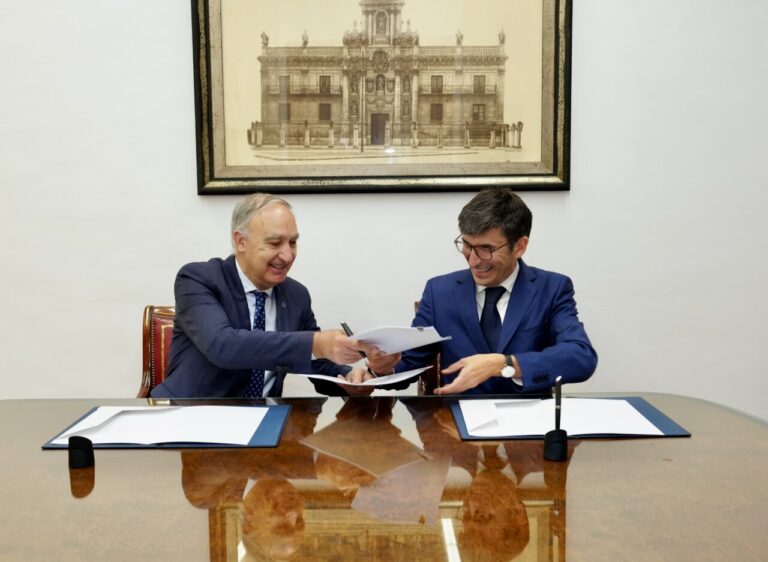 Dos hombres firmando un acuerdo en una mesa con documentos.