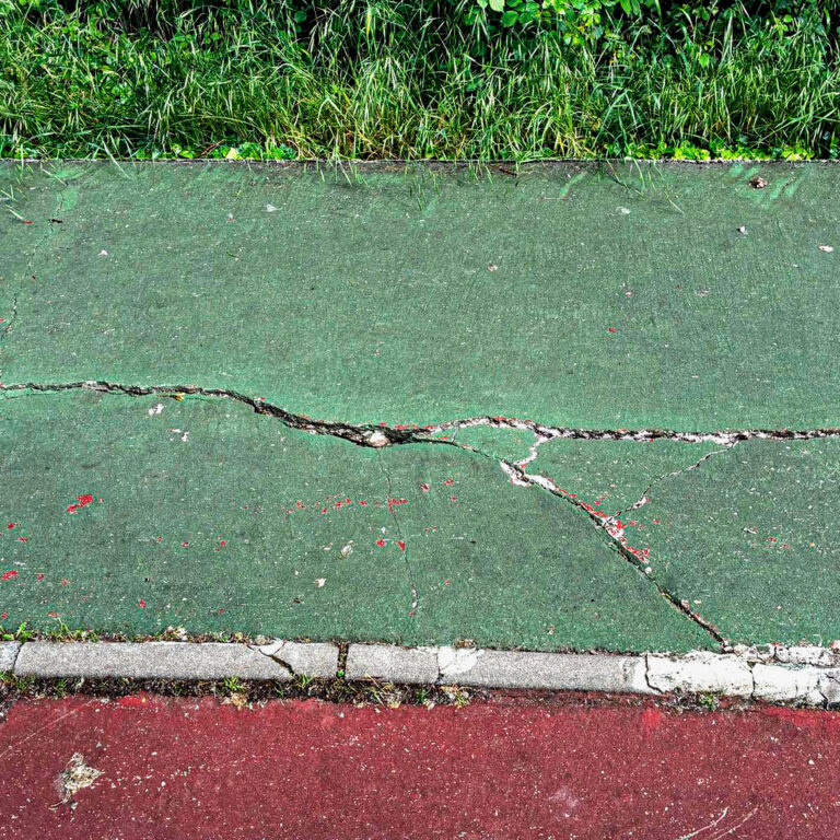 Pavimento dañado en un parque con hierba al fondo