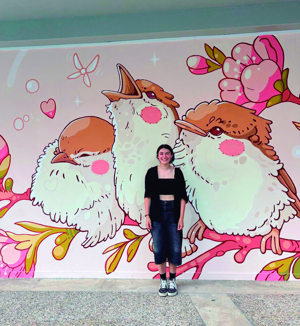 Nadia Bilbao posando frente a su mural de aves coloridas