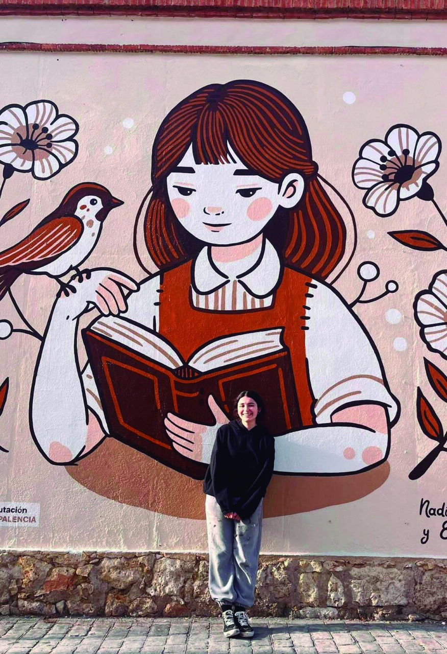 Nadia Bilbao posando frente a su mural de una chica leyendo