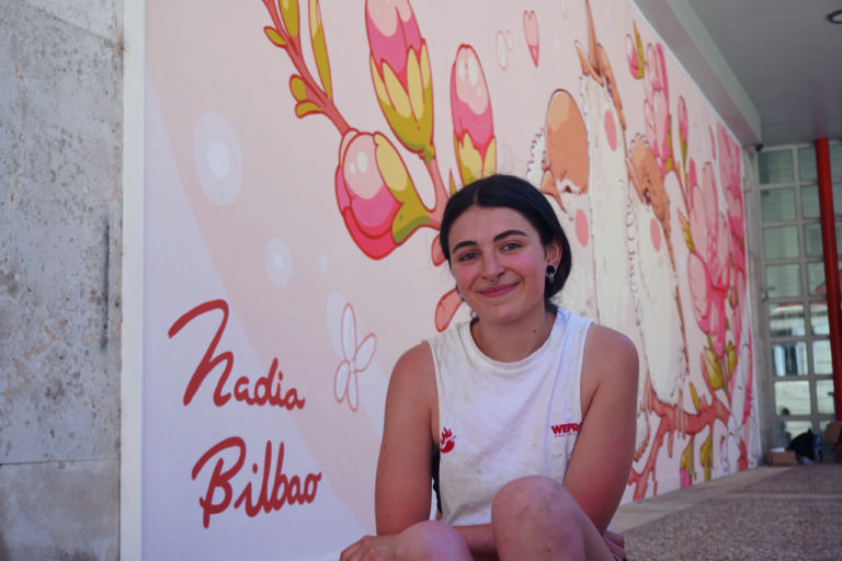 Nadia Bilbao, joven artista muralista sonriente frente a su obra