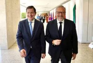 Dos hombres sonrientes caminando en un pasillo con banderas al fondo
