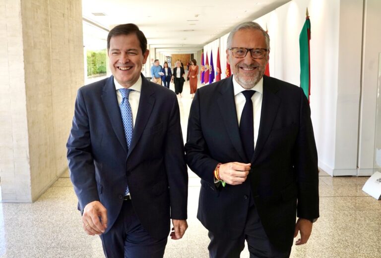 Dos hombres sonrientes caminando en un pasillo con banderas al fondo