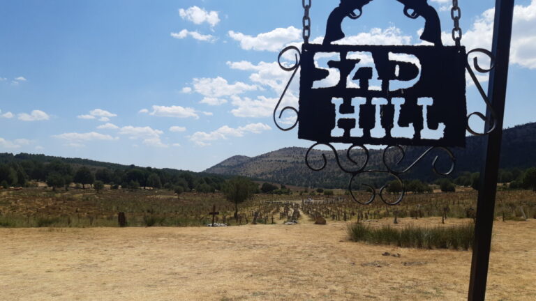 Cartel de Sad Hill con un paisaje árido y montañas al fondo