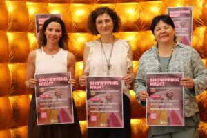 Tres mujeres sosteniendo carteles de la Showpping Night 2026 en un fondo dorado