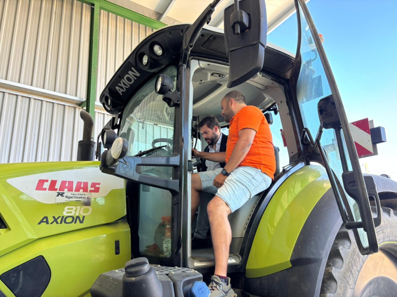 Dos hombres en la cabina de un tractor CLAAS AXION durante una visita agrícola.