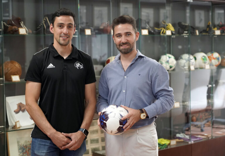 Dos hombres sosteniendo un balón de fútbol en un entorno deportivo