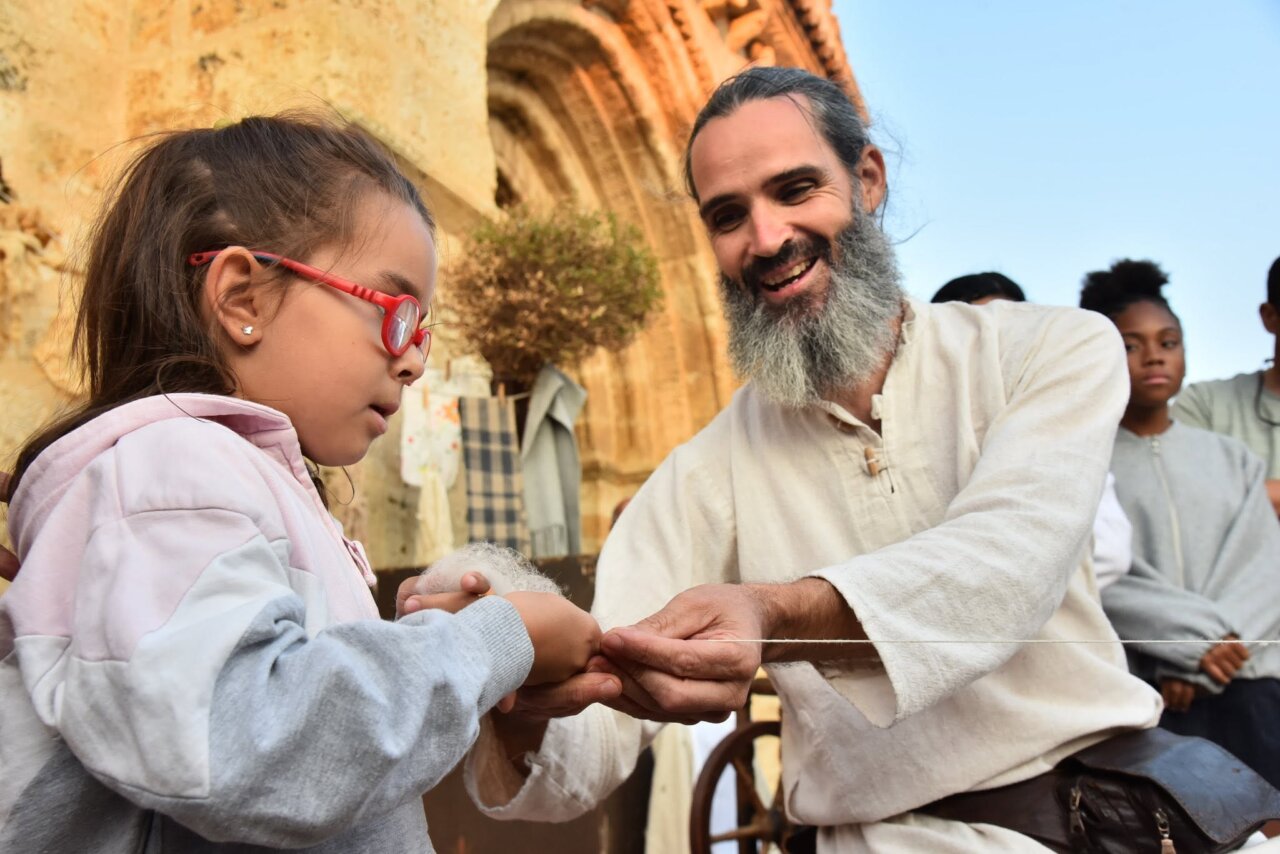 Niña con gafas rojas interactuando con adulto en representación histórica