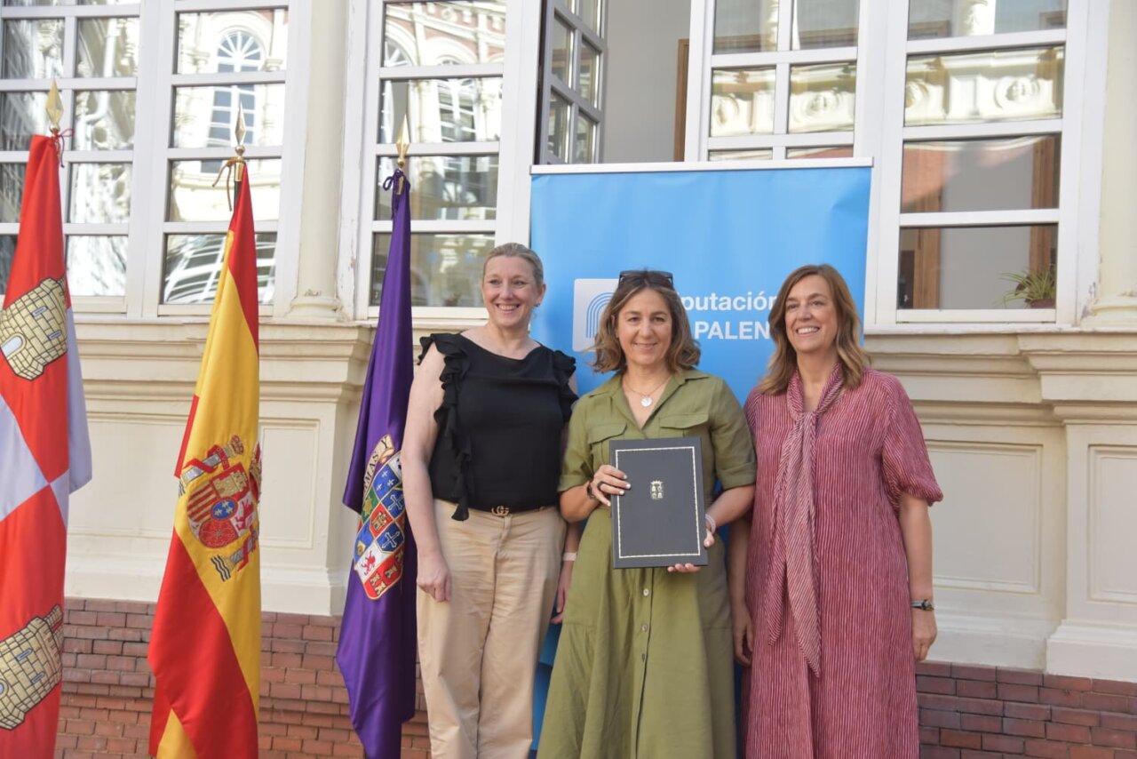 Tres mujeres posando con documentos en un evento sobre vivienda social