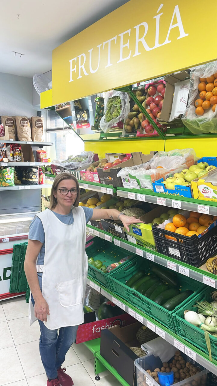 Mujer en frutería mostrando productos frescos en supermercado AMK.