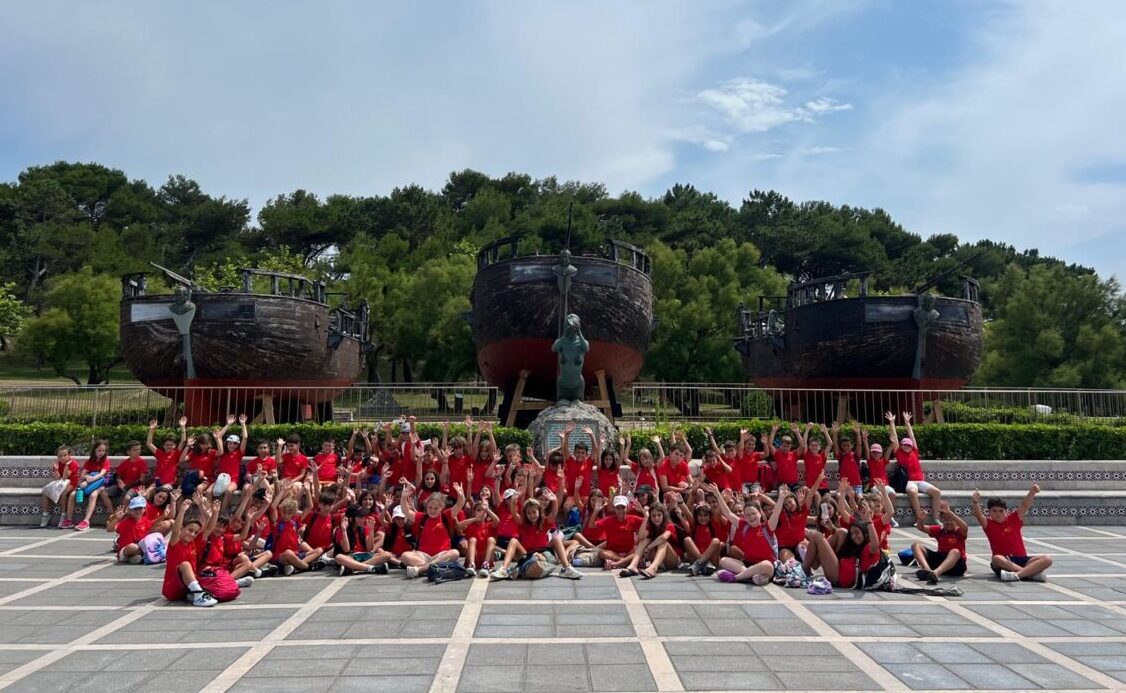 Grupo de niños con camisetas rojas en un parque con barcos de fondo