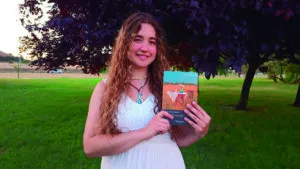 Joven poeta Eva Pérez Cepeda sosteniendo su libro en un entorno natural