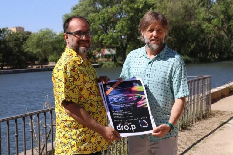 Dos hombres sosteniendo un cartel del festival DRO.P junto a un río