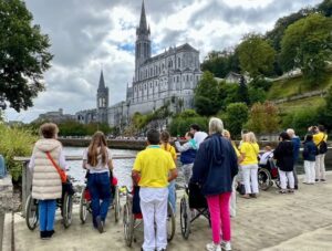 Grupo de personas en sillas de ruedas en Lourdes frente a un santuario
