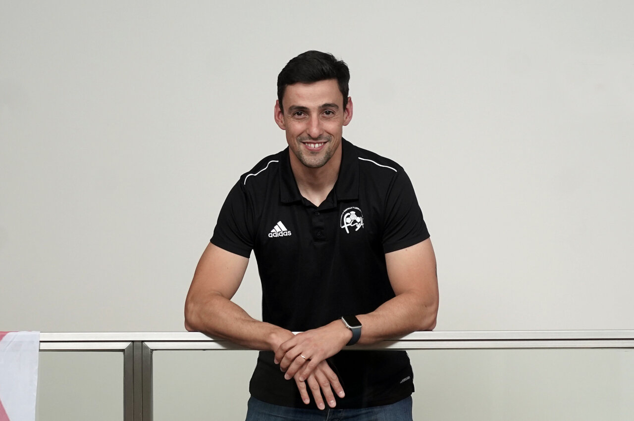 Entrenador de fútbol sonriente en camiseta negra apoyado en barandilla