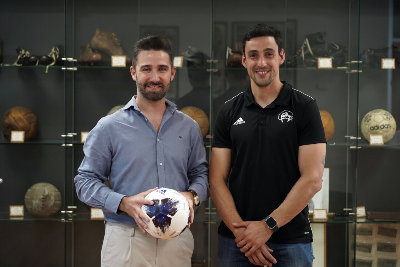 Dos hombres posando con un balón de fútbol en un museo deportivo