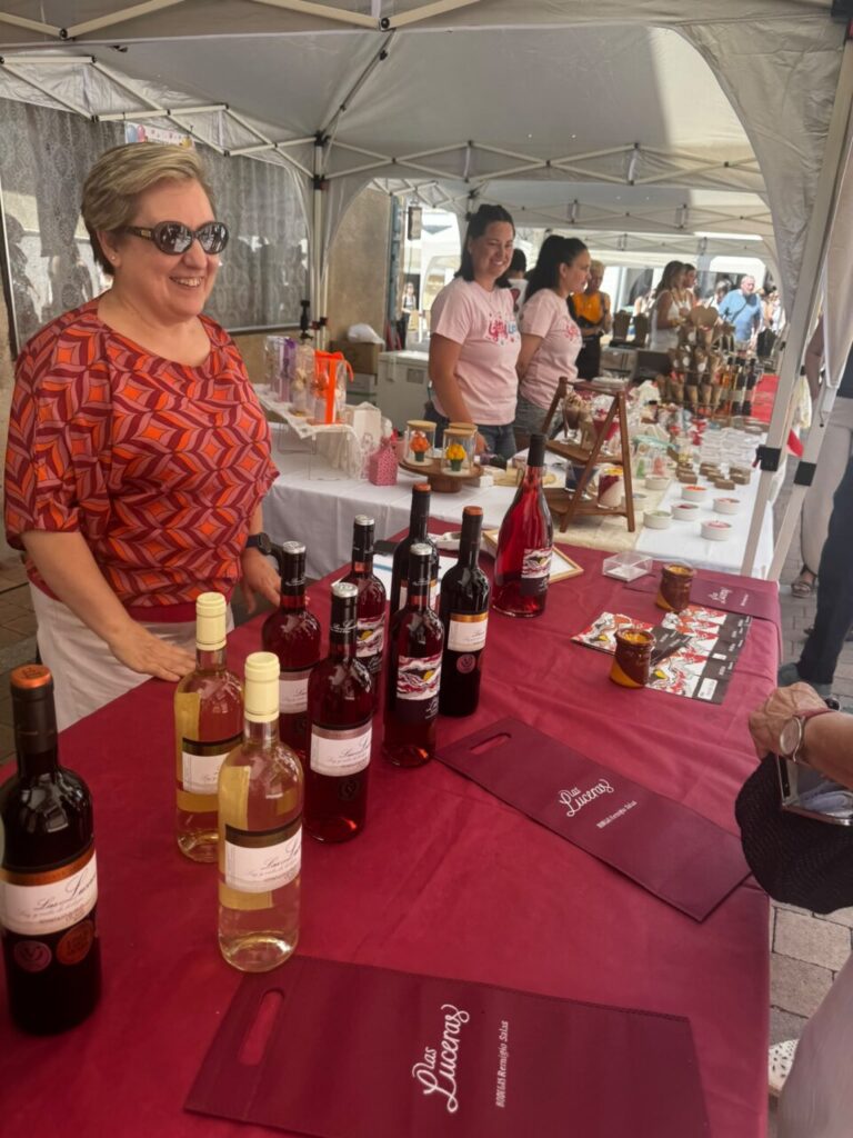 Mujer sonriente en un puesto de feria con vinos y productos locales