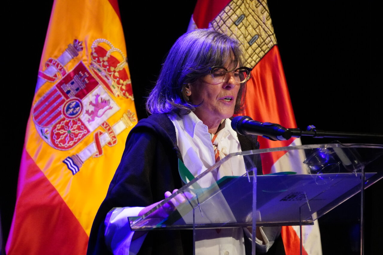 Mujer dando un pregón literario en un escenario con banderas