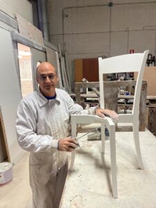 Hombre aplicando barniz a una silla blanca en un taller de muebles