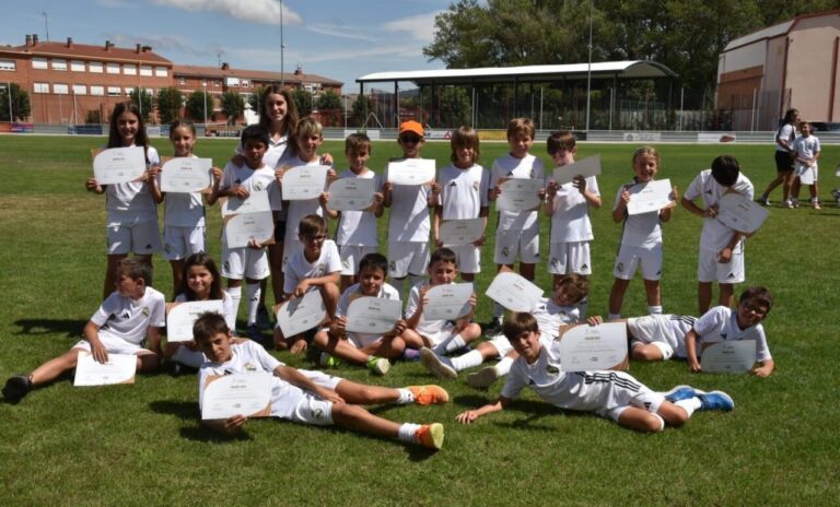 Grupo de niños con camisetas del Real Madrid sosteniendo diplomas en un campo de fútbol