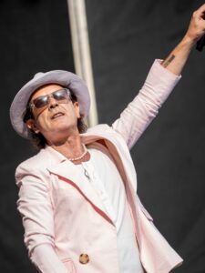 Coti actuando en un concierto con chaqueta rosa y sombrero