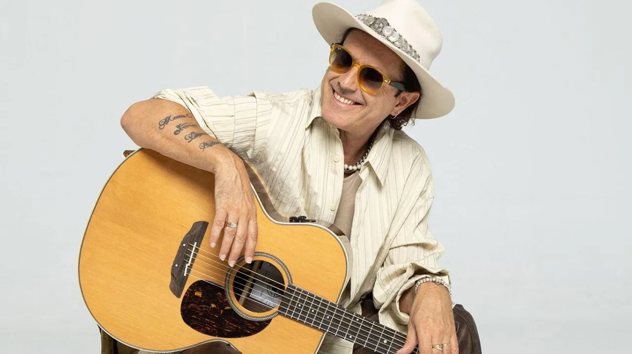 Coti sonriente con guitarra en un fondo claro
