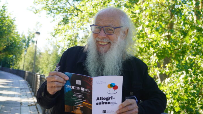 Dimas González sonriente sosteniendo un folleto de Allegríssimo en un parque.