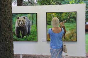 Mujer observando pinturas de un oso y un ciervo en una exposición de arte