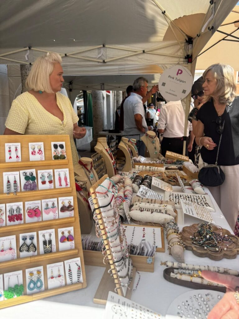 Mujeres conversando en un mercado con bisutería y artesanía