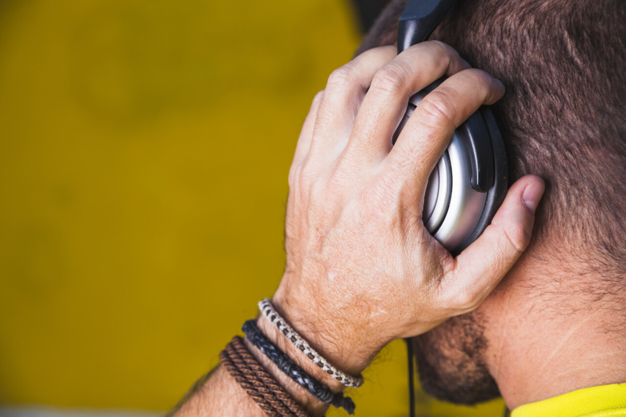 Hombre anónimo escuchando música con auriculares en un fondo amarillo