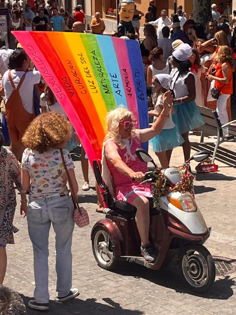 Persona con peluca rubia y bandera de colores en desfile festivo