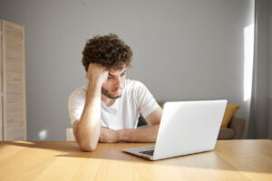Joven frustrado con barba ligera trabajando en computadora portátil