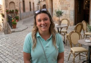 Mujer sonriente en una plaza con mesas y sillas vacías