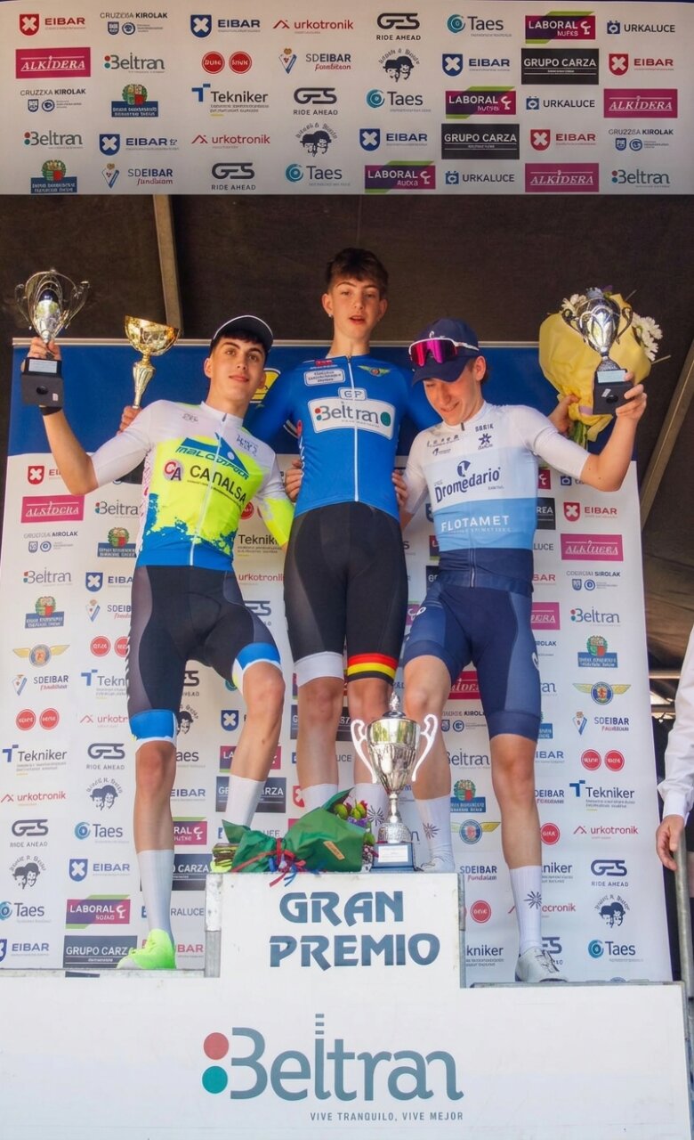 Tres ciclistas en el podio con trofeos en un evento deportivo