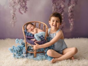 Niño sonriente junto a un bebé dormido en una silla de mimbre