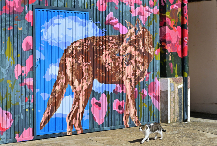 Mural colorido con un gato caminando frente a una pintura de un animal.